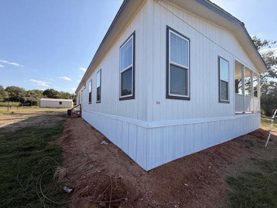 A white manufactured home with crisp white skirting wrapping the corner, on freshly graded red earth.