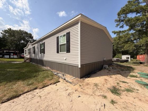 The gable end of a tan home with brown skirting following the slope of the yard.