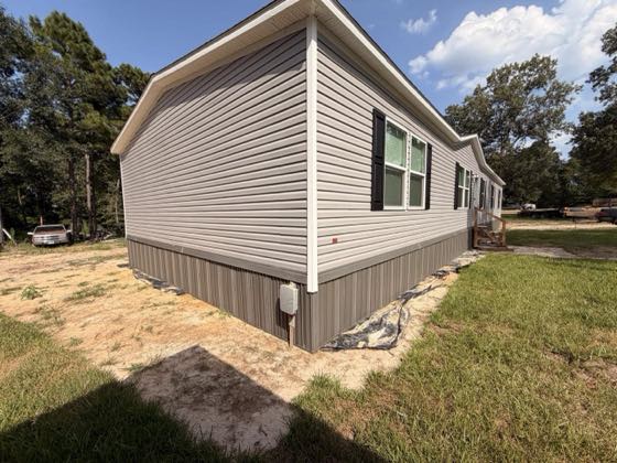 A grey-tan home with brown skirting closing the gap down to sandy ground.