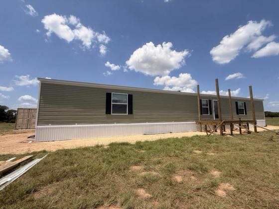 A sage green home with an access ramp and white skirting across the front.