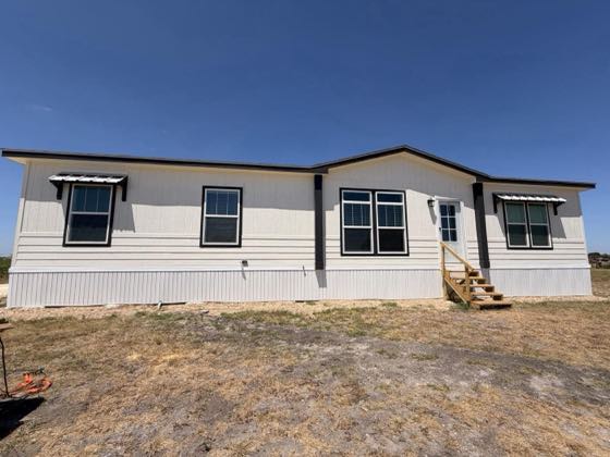 The front of a white home with black trim and window awnings, finished with white skirting.