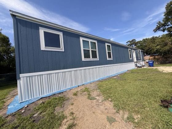 A blue manufactured home finished with white skirting on a green lot.