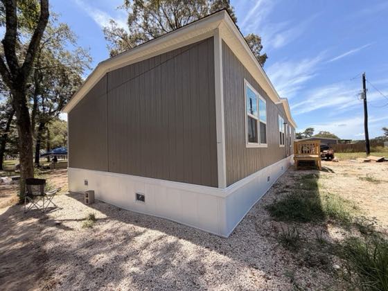 The gable end of a tan home with white skirting on a gravel bed.