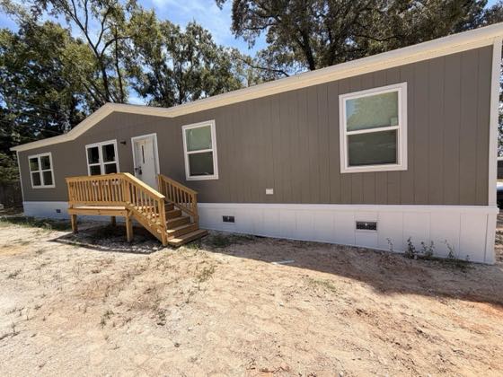 A tan manufactured home with white skirting, a wooden deck and stair at the door.