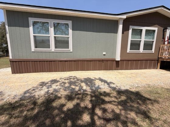 A sage green home with dark brown skirting, finished on a gravel drive.