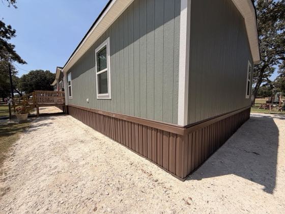 The corner of a sage green home with brown skirting turning the angle.